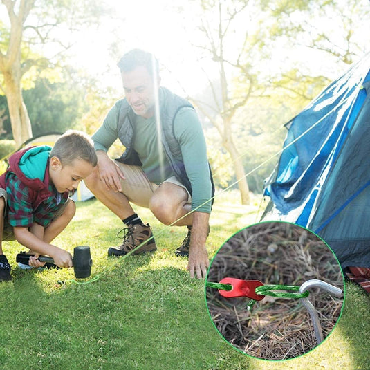 Een man en kind zetten een blauwe tent op gras op voor hun kampeeravonturen. Het kind gebruikt een hamer op een tentharing; in de inzet is de vastgehaakte scheerlijn te zien met hoogwaardige aluminium nylon kwaliteit van "Laat je tent stevig staan met onze reflecterende scheerlijn touwen!" Felle zon filtert door bomen.
