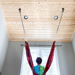 Load image into Gallery viewer, In een rode hangmat binnenshuis geniet men van het zonlicht dat door het houten plafond filtert, dankzij De ultieme 360° draaibare plafondhaak voor maximale veelzijdigheid en veiligheid, die een veilig en panoramisch uitzicht op de rustige omgeving mogelijk maakt.
