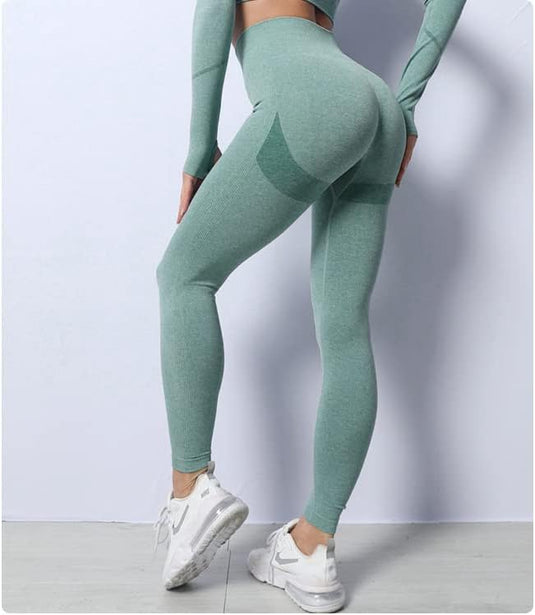 De persoon is elegant zijwaarts geposeerd, balancerend op één voet in witte sneakers tegen een witte achtergrond. Ze presenteren een blauwgroen yoga-workoutset, met een tijdelijke legging gemaakt van bestendige stof voor comfort en stijl, onderdeel van de 3-delige set "Zie er geweldig uit en voel je geweldig".