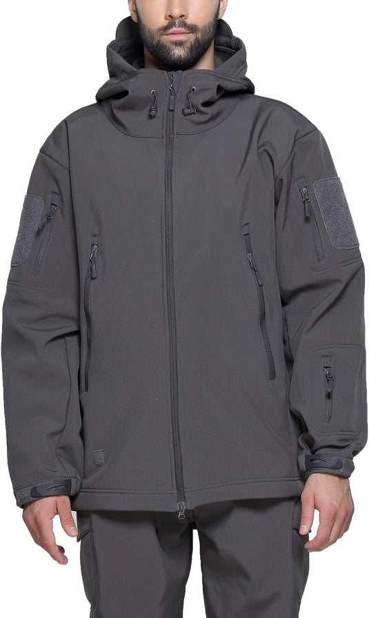 Een persoon staat op een witte achtergrond en draagt de Camouflage tactische heren softshell jas, ideaal voor buitenavonturen, in donkergrijs met meerdere ritsen, zakken en een capuchon, gecombineerd met bijpassende broek.