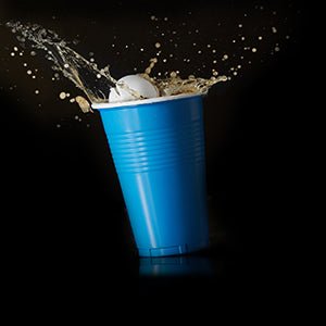 Laad afbeelding in Galerijviewer, In een zwarte achtergrond spat een van de 100 veelzijdige bierpongballetjes uit de set &quot;Speel, daag uit en knutsel&quot; in een blauwe plastic beker gevuld met vloeistof.
