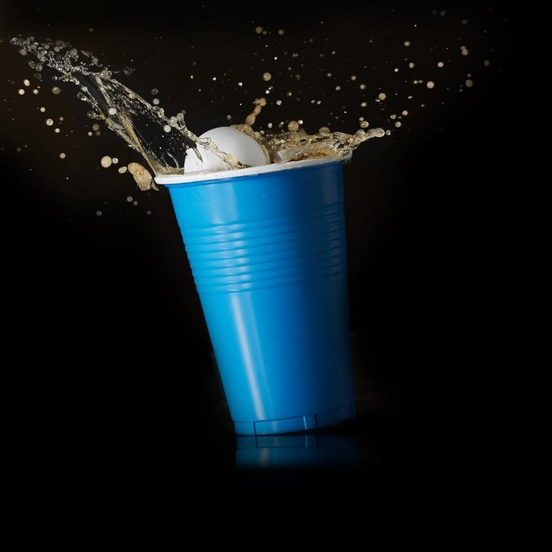 Laad afbeelding in Galerijviewer, Een pingpongbal spat in een blauwe beker met vloeistof tegen een zwarte achtergrond, wat een weerspiegeling is van een bierpongballetspel en het veelzijdige gebruik ervan in leuke drinkspelletjes benadrukt. Ontdek dit met de set &quot;Speel, dag uit en knutsel met deze uitgebreide set van 100 bierpongballetjes!.
