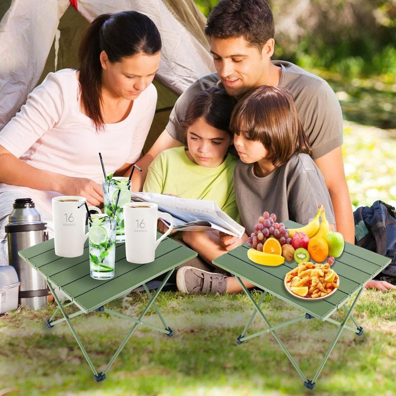 Load image into Gallery viewer, Een gezin geniet van een boek bij hun tent, zittend op het gras. Vooraan staan twee opvouwbare tafels met drankjes, fruit en snacks te midden van zonnig groen. Hun ultralichte draagbare kampeertafel van Ontdek heeft een antislip voetdopontwerp voor extra stabiliteit.
