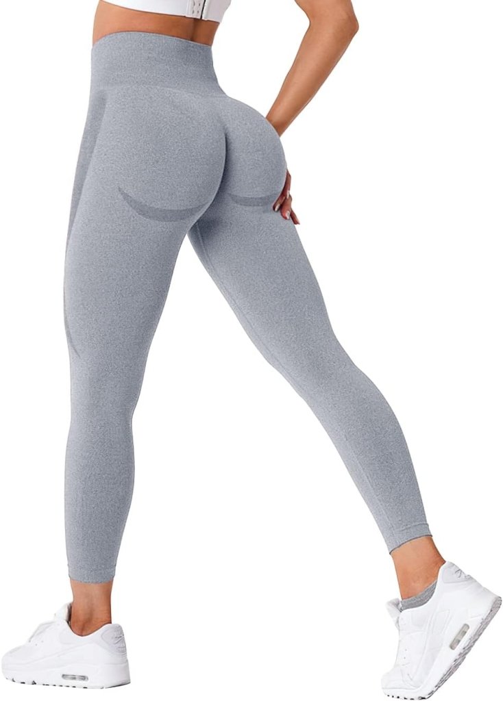 Load image into Gallery viewer, Een persoon staat dynamisch in het grijs &quot;Ervaar ultiem comfort en stijl met onze compressie sportlegging!&quot; met een geplooid billenontwerp en witte sneakers, wegkijkend.

