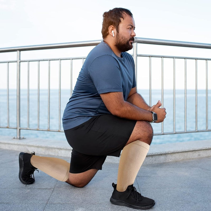 Load image into Gallery viewer, Een man in sportkleding knielt aan de waterkant, met een koptelefoon en een smartwatch op. Met &quot;Verbeter prestaties en herstel met compressiesokken voor dames en heren - Maat S/M tot 7XL!&quot; op zijn benen richt hij zich op spierherstel en het verbeteren van zijn bloedsomloop voor optimale prestaties.
