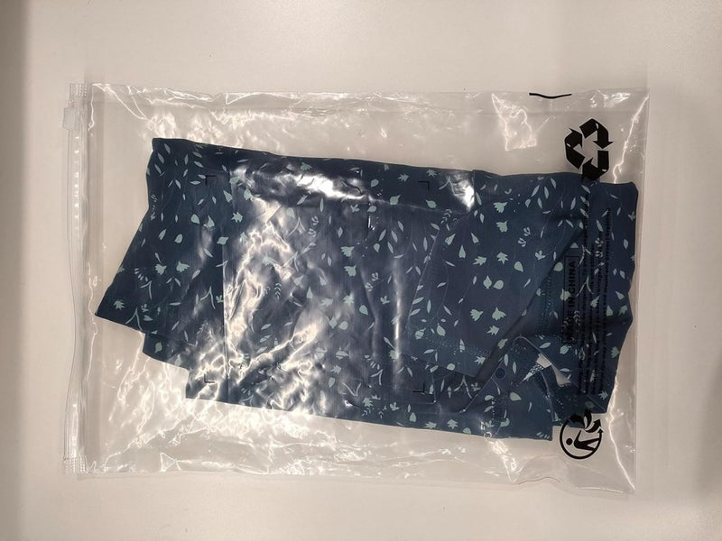 Laad afbeelding in Galerijviewer, Het product &quot;Sportieve en stijlvolle golfskort voor dames&quot; is gemaakt van een blauwe bloemenstof, netjes opgevouwen in een doorzichtige hersluitbare plastic zak op een witte ondergrond.
