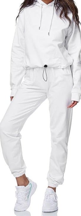 Laad afbeelding in Galerijviewer, Een persoon draagt een witte hoodie en een joggingbroek, met daarop het logo &quot;Dames joggingpak: Comfort en stijl in één&quot;. Hij draagt daarbij witte sneakers tegen een effen achtergrond voor een stijlvolle en comfortabele look.
