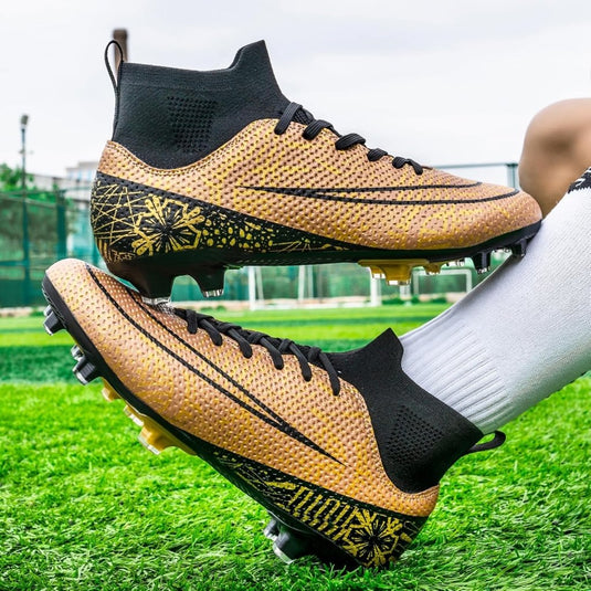 Een persoon met witte sokken benadrukt het hoge ontwerp van "⚽ Domineer het veld met deze hoogwaardige voetbalschoenen!" door een gouden schoen met zwarte patronen en veters omhoog te houden op het gras, wat blijk geeft van verbeterde grip en stabiliteit.
