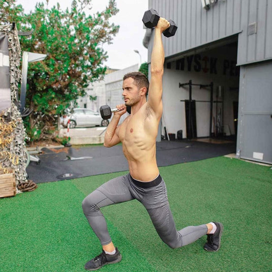 Een man in sportkleding voert een lunge uit in de buitenlucht, waarbij hij één arm boven zijn hoofd heft met de Ultieme hexagonale halter van 6 kg - perfect voor krachtige trainingen!.
