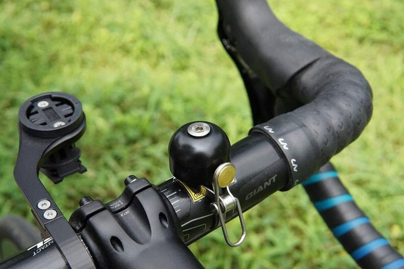 Load image into Gallery viewer, Close-up van een fietsstuur met de Stijlvol retro fietsbel en een lege apparaathouder. De getextureerde grip versterkt de klassieke uitstraling, tegen een weelderige groene grasachtergrond die de tijdloze charme versterkt.
