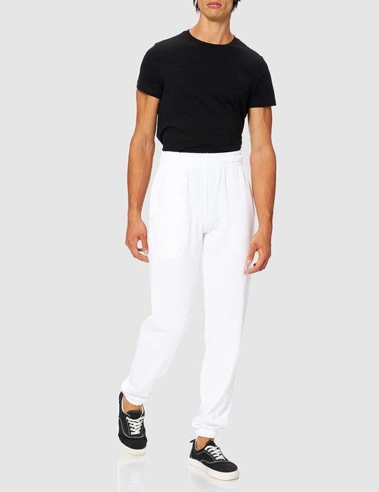 Een persoon met een zwart T-shirt, Comfortabele en stijlvolle heren joggingbroek – Jouw dagelijkse essential en zwarte sneakers met witte zolen staat tegen een effen grijze achtergrond.