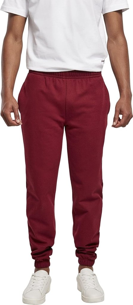 Een persoon in een wit overhemd, bordeauxrode "Comfortabele en stijlvolle heren joggingbroek – Jouw dagelijkse essential", en witte sneakers poseert tegen een frisse witte achtergrond.