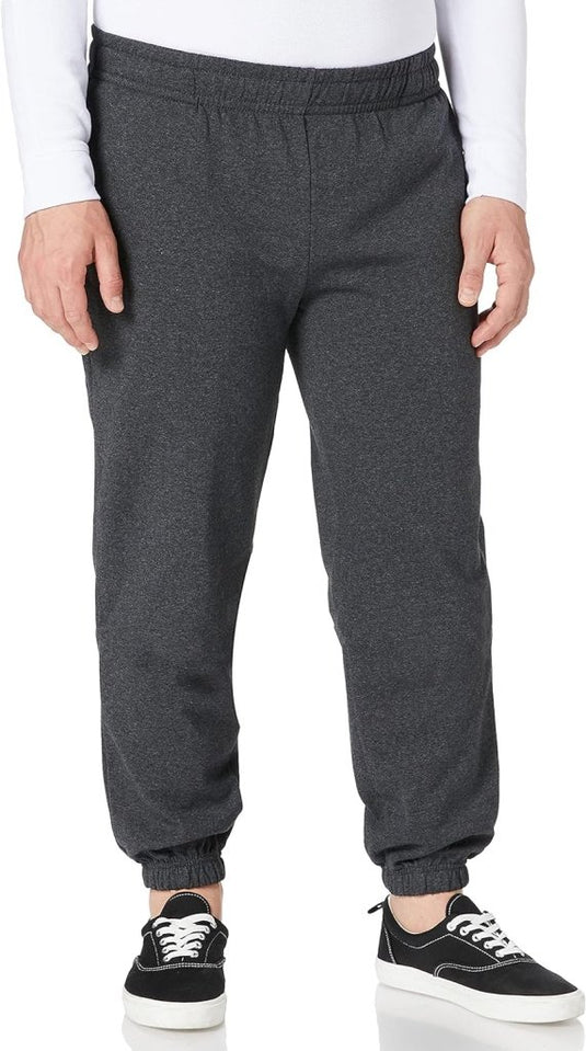 Een persoon staat tegen een witte achtergrond en draagt een wit shirt met lange mouwen, een donkergrijze JouDagelijkse heren joggingbroek voor ultiem comfort en zwarte sneakers met witte zolen, die een moeiteloze stijl uitstralen.