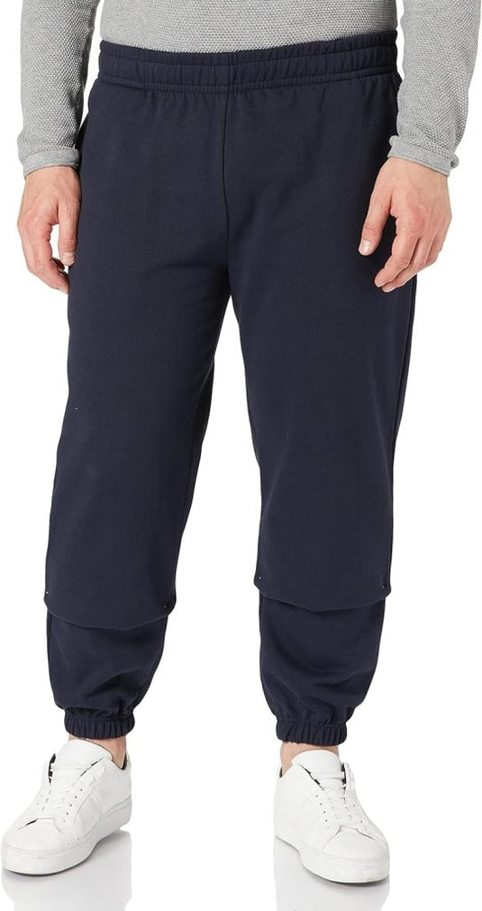 Een persoon draagt een grijs shirt met lange mouwen, de "Comfortabele en stijlvolle heren joggingbroek – Jouw dagelijkse essential" in marineblauw voor comfort en stijl, en witte sneakers tegen een effen achtergrond.