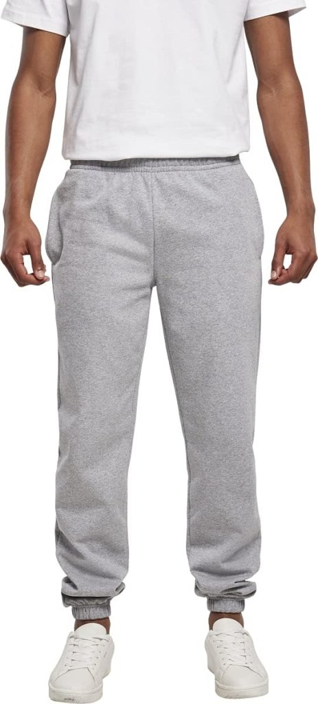 Iemand belichaamt comfort en stijl in Comfortabele en stijlvolle heren joggingbroeken – Jouw dagelijkse essential in grijs, gecombineerd met een wit t-shirt en frisse witte sneakers, tegen een effen achtergrond.