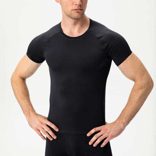 Een persoon die een getailleerd zwart "Verbeter je prestaties met dit geweven compressieshirt voor heren" draagt, met de handen op de heupen, staat tegen een effen achtergrond en straalt vertrouwen uit en bereidheid tot spierherstel.