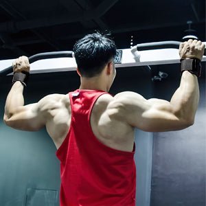 Een persoon die "Stevige hefbanden voor maximale kracht en ondersteuning" gebruikt in een rode tanktop, voert een pull-up uit in een sportschool, van achteren gezien, waarbij zijn gespierde armen en rug zichtbaar zijn tijdens krachttraining.