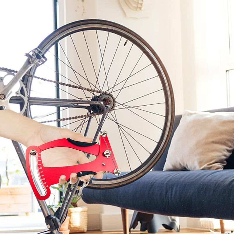 Load image into Gallery viewer, Een hand houdt de 🔧 Ontmoet en optimaliseer je fietsspanning met deze spaakspanningsmeter! vlakbij een omgekeerde fiets binnenshuis met een bank op de achtergrond, klaar om af te stemmen voor optimale wielprestaties.
