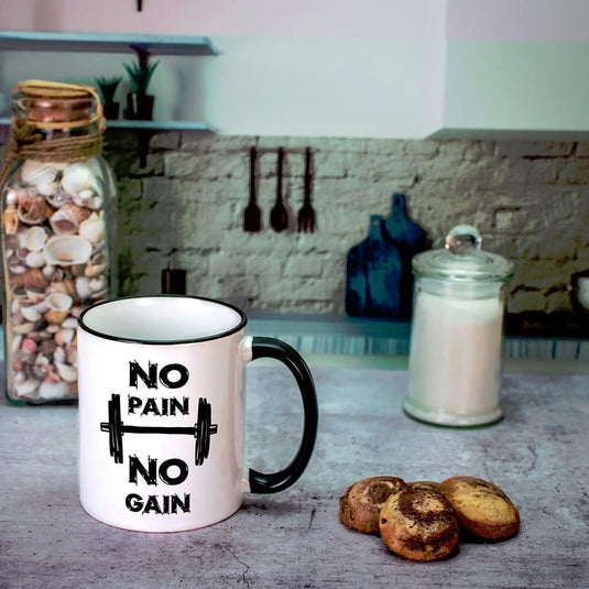De keramische mok "No Pain No Gain" met halterontwerp staat op het aanrecht, omringd door koekjes en potten. Vrijwel motiverend, het is vaatwasmachinebestendig en magnetronbestendig. Ervaar de perfecte start van je dag met deze praktische mok!.