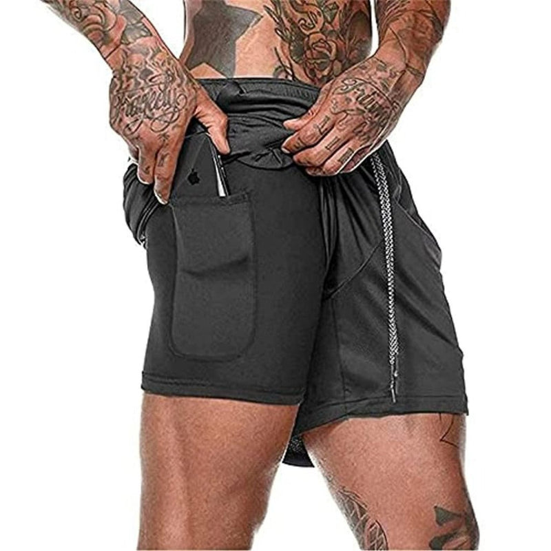 Laad afbeelding in Galerijviewer, Een getatoeëerde persoon schuift een smartphone in de zijzak van zijn comfortabele zwarte 2-in-1 short met trekkoord, gemaakt van sneldrogend materiaal, genaamd &quot;Ontdek het ultieme comfort en de functionaliteit van onze heren 2-in-1 shorts.

