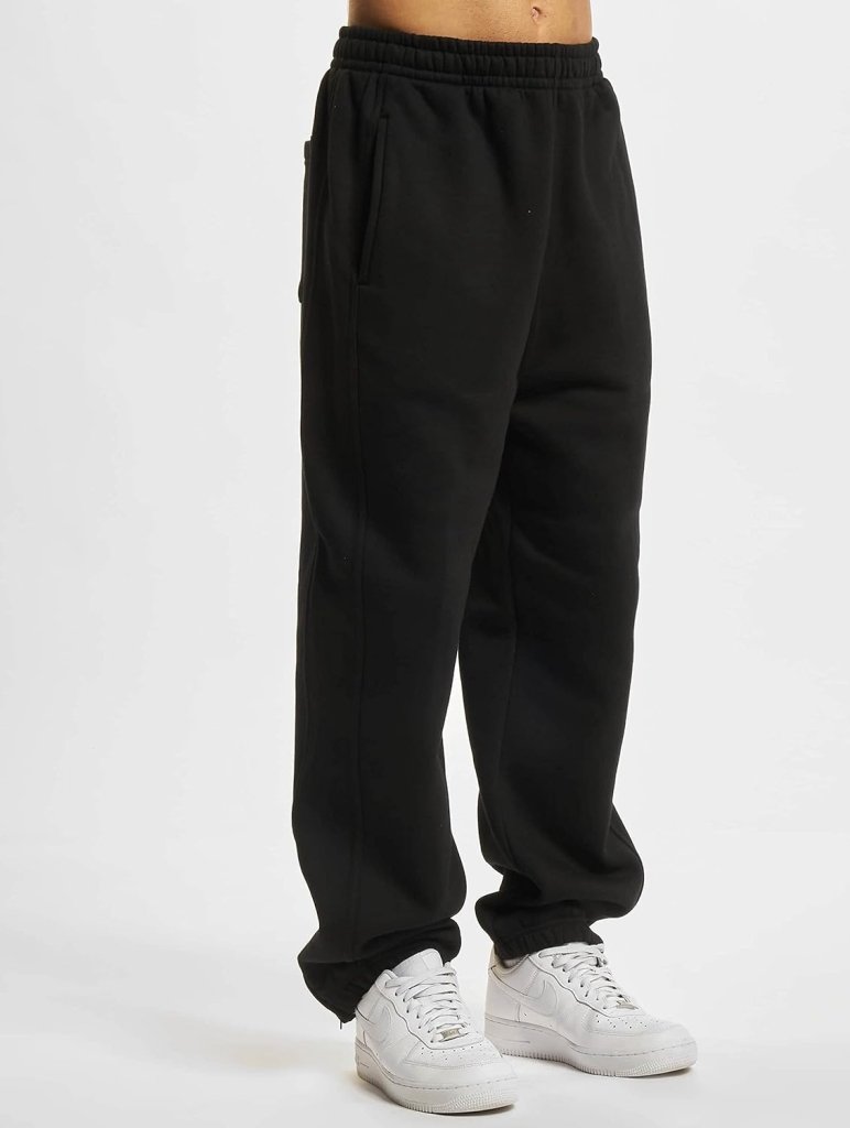 Laad afbeelding in Galerijviewer, Tegen een witte achtergrond draagt iemand de &quot;Comfortabele en stijlvolle joggingbroek voor heren&quot; in het zwart, met een nonchalante slanke snit. In combinatie met frisse witte sneakers combineert deze look moeiteloos stijl met comfort.
