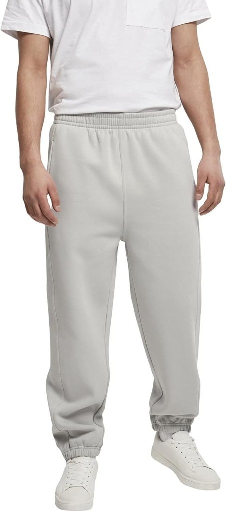 Laad afbeelding in Galerijviewer, Tegen een effen achtergrond staat een persoon met een wit T-shirt, een comfortabele en stijlvolle joggingbroek voor heren in lichtgrijs en witte sneakers.
