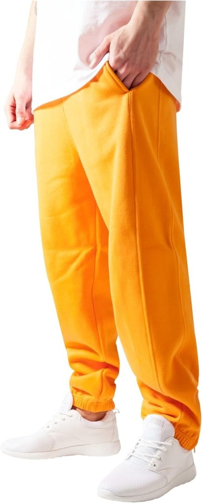 Laad afbeelding in Galerijviewer, Een persoon draagt een comfortabele herenjoggingbroek, geaccentueerd door feloranje en met een strakke pasvorm, gecombineerd met een wit overhemd en bijpassende sneakers tegen een effen achtergrond.
