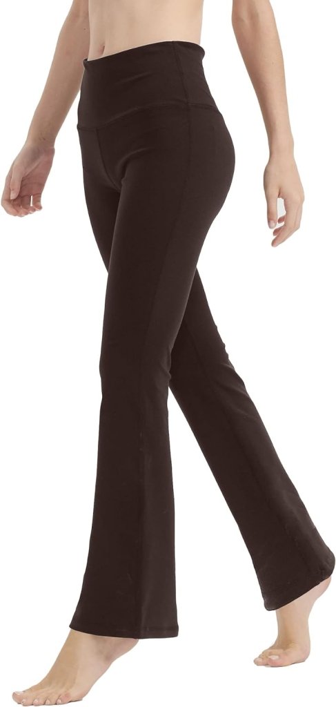 Een persoon loopt op blote voeten op een witte achtergrond en draagt een hoog getailleerde, zwarte, uitlopende yogabroek voor vrouwen, ontworpen voor perfecte buikcontrole en comfort.