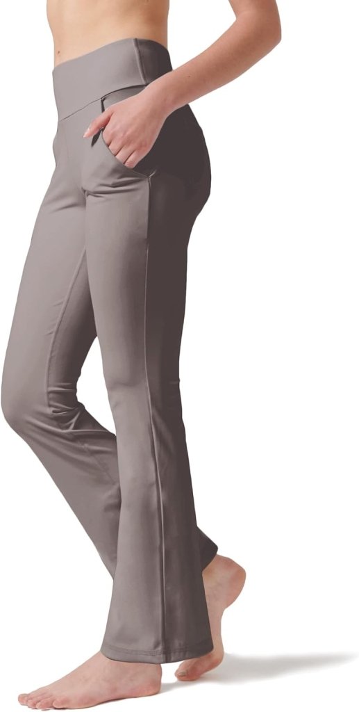 Een persoon staat blootsvoets tegen een witte achtergrond, gekleed in een grijze Yoga broek voor vrouwen: Perfecte buikcontrole en comfort met de handen in de zakken.