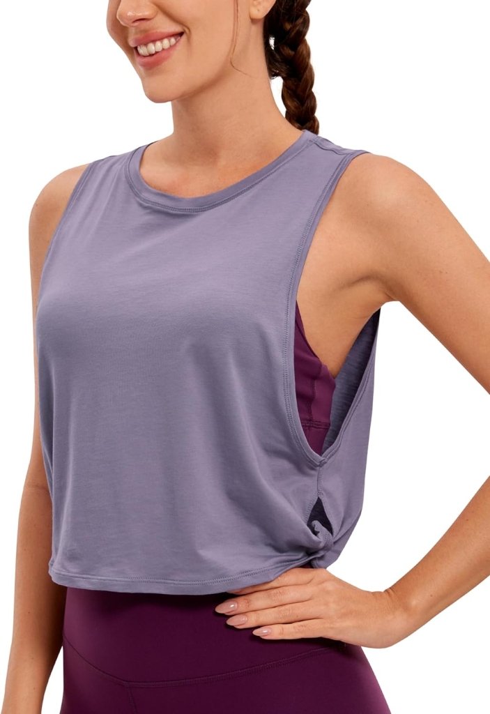 Laad afbeelding in Galerijviewer, Persoon draagt een Stijlvol en comfortabel: Yoga dames pima katoenen workout tank crop in lichtpaars over een donkerpaarse sportbeha en legging, haar in een vlecht, hand op de heup, lachend.
