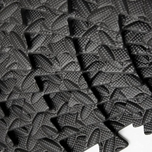 Close-up van een zwarte rubberen mat met driehoekige patronen en een antislipprofiel, perfect als beschermende puzzelmat voor fitnessapparatuur.