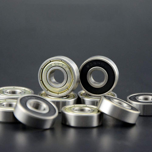 Een close-up van verschillende metalen kogellagers, waaronder koolstofstalen lagers met zwarte binnenringen, rustend op een donkere ondergrond. Deze 