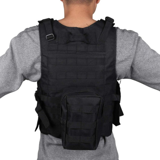 Een persoon modelleert het zwarte tactische vest "Ontketen je ware potentieel", met een achterzak en verstelbare bandjes, perfect voor paintball, terwijl hij een grijs shirt draagt.
