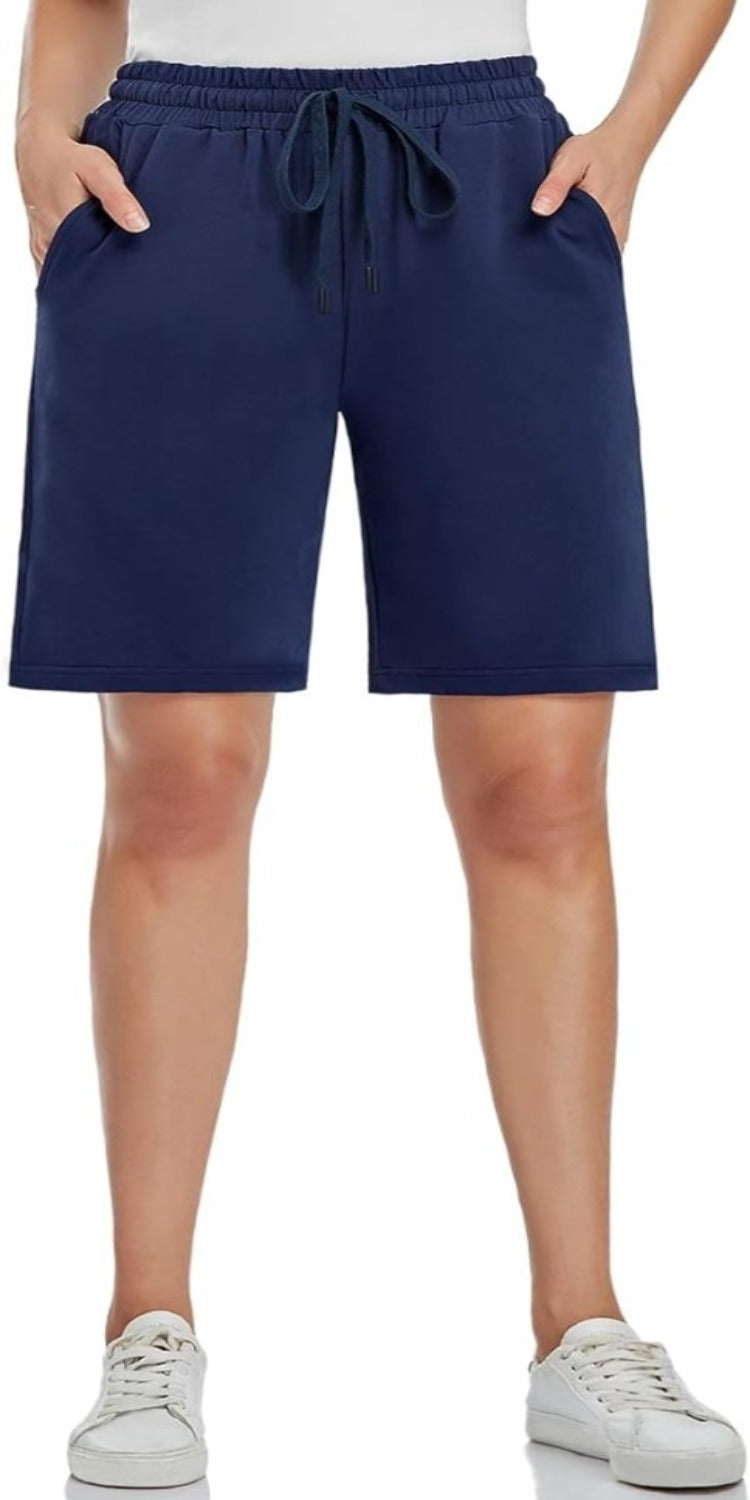 Laad afbeelding in Galerijviewer, Een persoon in de Bermudashort voor dames – comfortabel, veelzijdig en perfect voor elke gelegenheid – gecombineerd met witte sneakers, staat met de handen in de zakken. De short heeft een verstelbare tailleband voor een comfortabele pasvorm.
