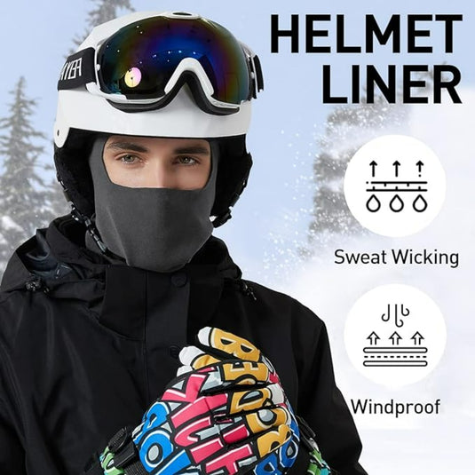 Gekleed in skikleding staat een persoon met een zweetafvoerende, winddichte helm en kleurrijke handschoenen in de sneeuw. De warme bivakmuts vult ze perfect aan en is ideaal voor buitenactiviteiten.