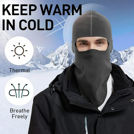Een persoon in een donkere bivakmuts staat tegen een besneeuwde bergachtergrond. De tekst luidt: "Blijf warm en comfortabel in de kou", met de nadruk op het winddichte ontwerp met iconen voor "Thermal" en "Breathe Freely". Perfect voor buitenactiviteiten.