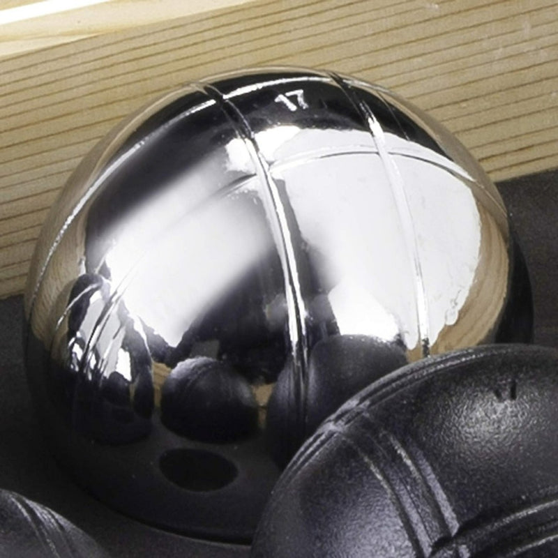 Load image into Gallery viewer, Op een donker oppervlak ligt een glimmende metalen petanquebal met gegraveerde lijnen, behorend bij het spel &quot;Ervaar petanque plezier met ons prachtige petanque spel in kist van hout&quot;, terwijl andere ballen gedeeltelijk zichtbaar zijn op de voorgrond.

