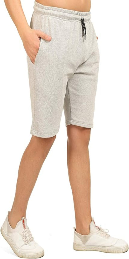 Tegen een witte achtergrond modelleert een persoon de comfortabele, gebruikelijke bermuda voor heren in lichtgrijze geweven stof, handen nonchalant in de zakken, gecombineerd met witte sneakers.