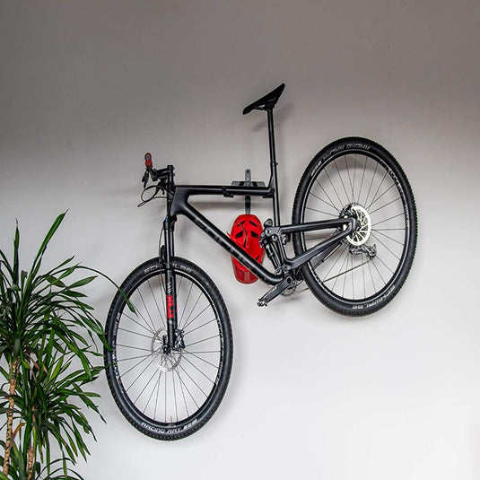 Aan het ‘Optimaliseer je ruimte met onze stijlvolle fiets ophangsysteem’ hangt een zwarte mountainbike, met daaraan een rode helm. Een groene plant geeft links een natuurlijk tintje.