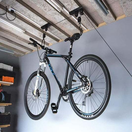 Een zwart-witte mountainbike wordt ondersteboven aan het plafond van een garage gehangen met behulp van de "Optimaliseer uw ruimte en bescherm uw fiets met de innovatieve fietslift.