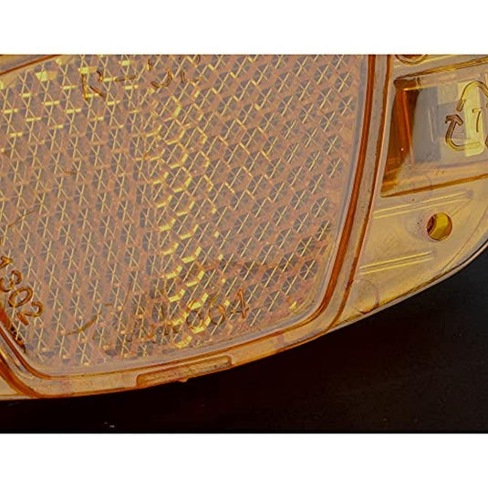 Een close-up van een amberkleurige fietsreflector met een gestructureerd oppervlak en een schroef aan de rand, wat de veiligheid en zichtbaarheid tegen een donkere achtergrond vergroot, zoals te zien in de Verhoog je zichtbaarheid in het donker met de fiets reflectorset!.