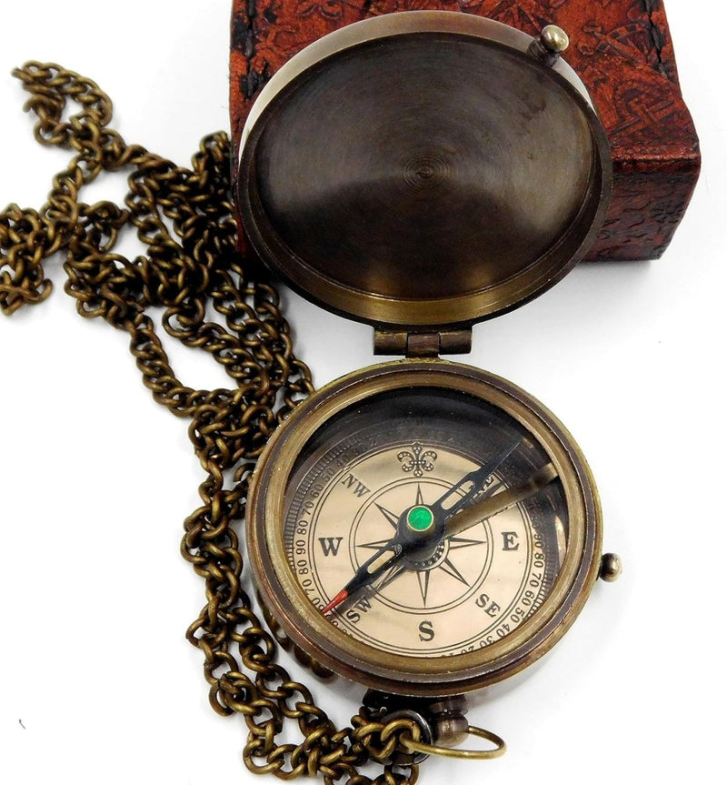 Laad afbeelding in Galerijviewer, Een &quot;Handgemaakt messing zakkompas: een klassieke must-have voor outdoorliefhebbers&quot; met een lange ketting, wijzend naar het noorden, rust elegant voor het uitgesneden houten kistdeksel.

