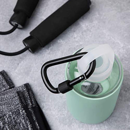 Een springtouw, een grijze handdoek en een groene waterfles met Veiligheid en veelzijdigheid onderweg: Ontdek onze hoogwaardige aluminium karabijnhaken rusten op een grijze ondergrond, ideaal voor buitenactiviteiten.
