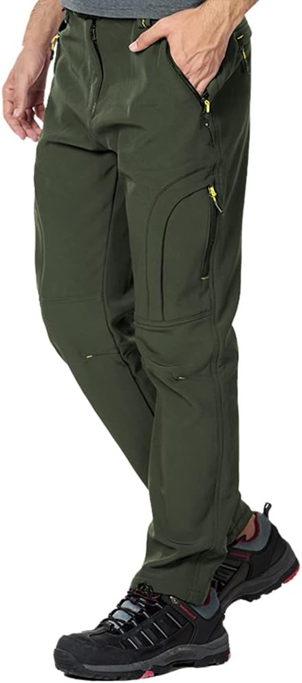 Een persoon draagt de groene Houd je warme en comfortabele wandel- en skibroek, met meerdere zakken met ritssluiting, ontworpen om winddicht en droog te zijn, moeiteloos te combineren met zwarte wandelschoenen.
