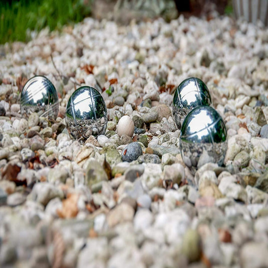 De "Beleef plezier en verbinding overal met onze hoogwaardige jeu de boules-set!" liggen verspreid op kiezelstenen buiten: vier zilveren balletjes en een klein wit doelbal, klaar voor een potje jeu de boules onder de blote hemel.