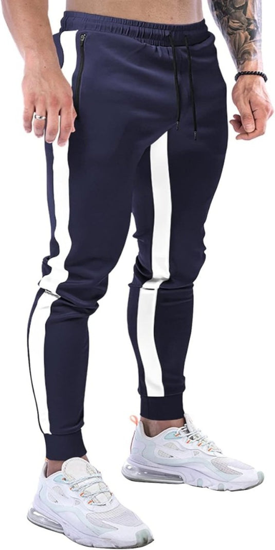 Een man die een marineblauwe joggingbroek voor heren draagt met witte zijstrepen en witte sneakers straalt een stijlvolle uitstraling uit, waarbij zijn getatoeëerde arm goed tot zijn recht komt.