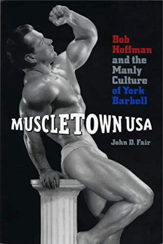 Een bodybuilder poseert op een voetstuk voor de cover van "John D. Fair: Muscletown USA" en onderzoekt de belangrijke invloed van Bob Hoffman en York Barbell op gewichtheffen en de mannelijke cultuur.