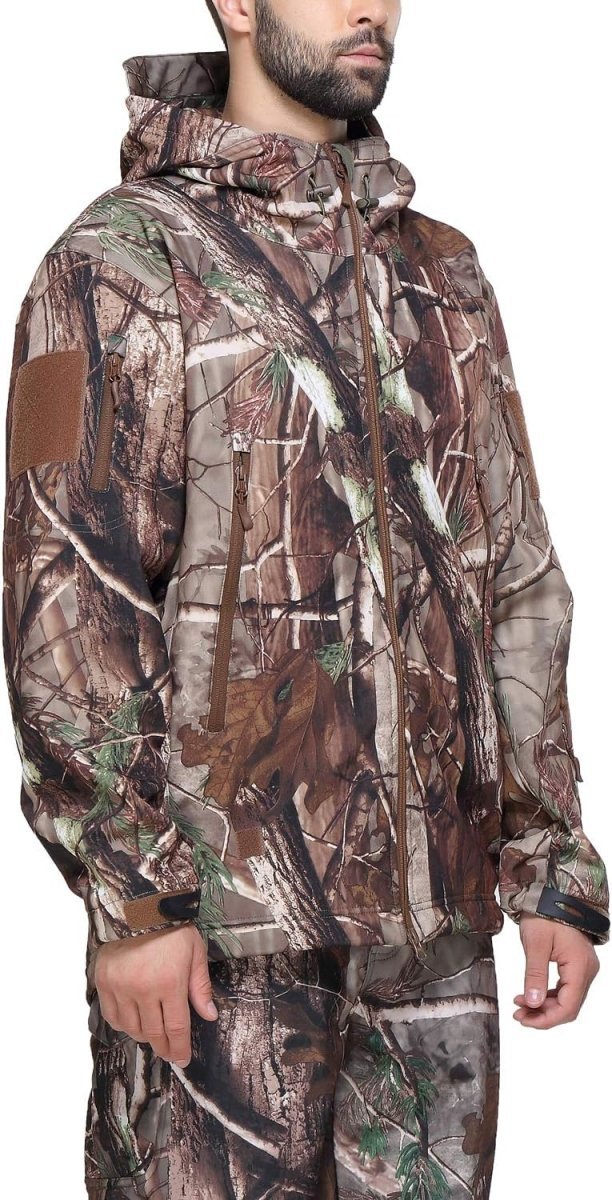 Laad afbeelding in Galerijviewer, Een persoon die een Camouflage tactische heren softshell jas en bijpassende broek draagt, met een boom- en bladpatroon, straalt zowel stijl als functionaliteit uit voor buitenavonturen.
