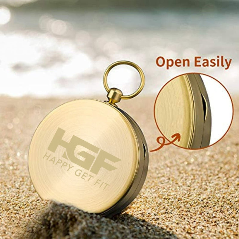 Laad afbeelding in Galerijviewer, Een rond, gouden zakhorloge dat lijkt op het Happygetfit kompas is half begraven in het zand. Een close-up inzet benadrukt de rand van het horloge, met &quot;Open Easily&quot; en &quot;HGF Happy Get Fit&quot; op de wijzerplaat.
