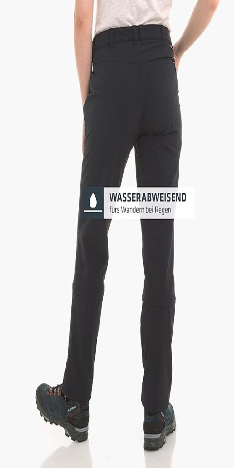 Laad afbeelding in Galerijviewer, A person in black Ontdek de perfecte wandelbroek voor dames, ideaal voor regenachtig weer, met waterafstotende stof, 4-way stretch en S.Café ICE-CAFÉ technologie voor topcomfort en prestatie, staat met handen in zakken laarzen te dragen. Duitse tekst benadrukt geschiktheid voor natte omstandigheden.
